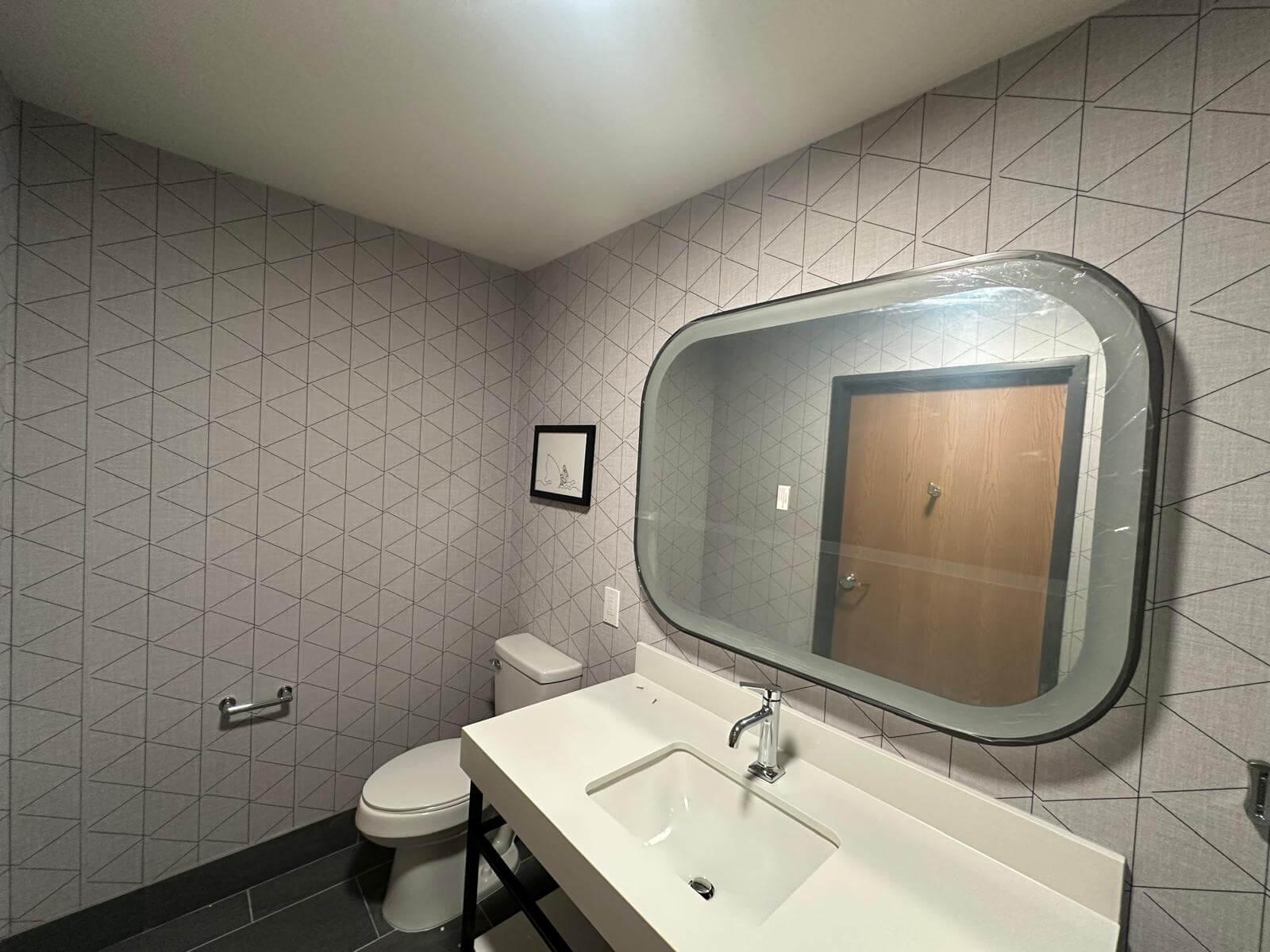 Bathroom sink and mirror surrounded by walls with triangle pattern wallpaper.
