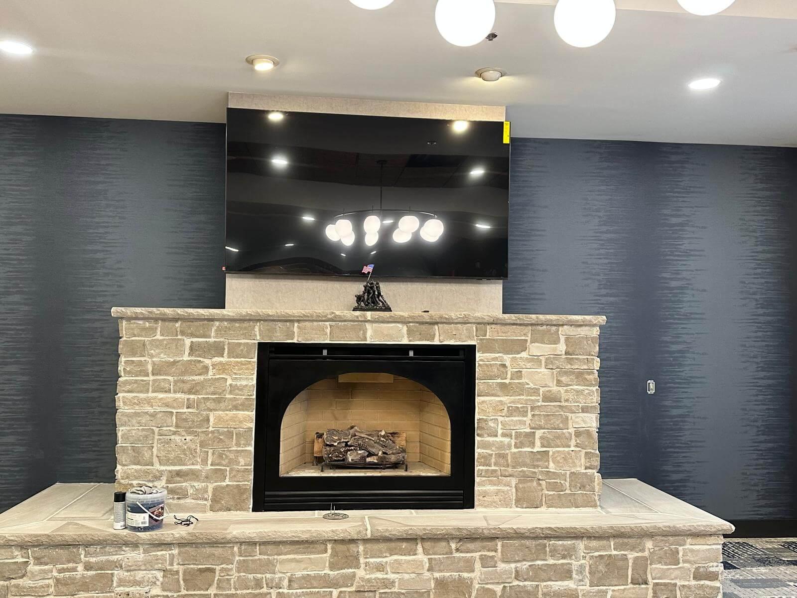 Fireplace with TV above it and wall behind it has simple black wallpaper.