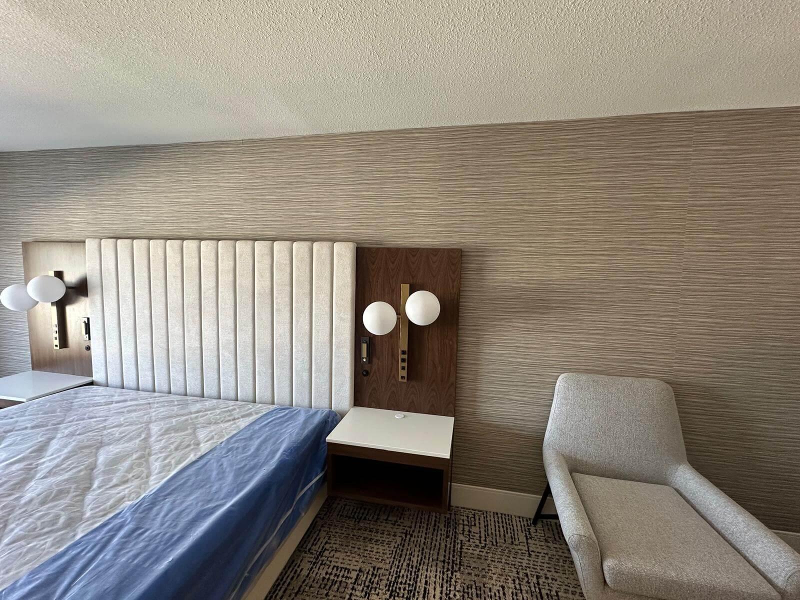 Hotel room with bed and a neutral horizontal wallpaper on the walls.