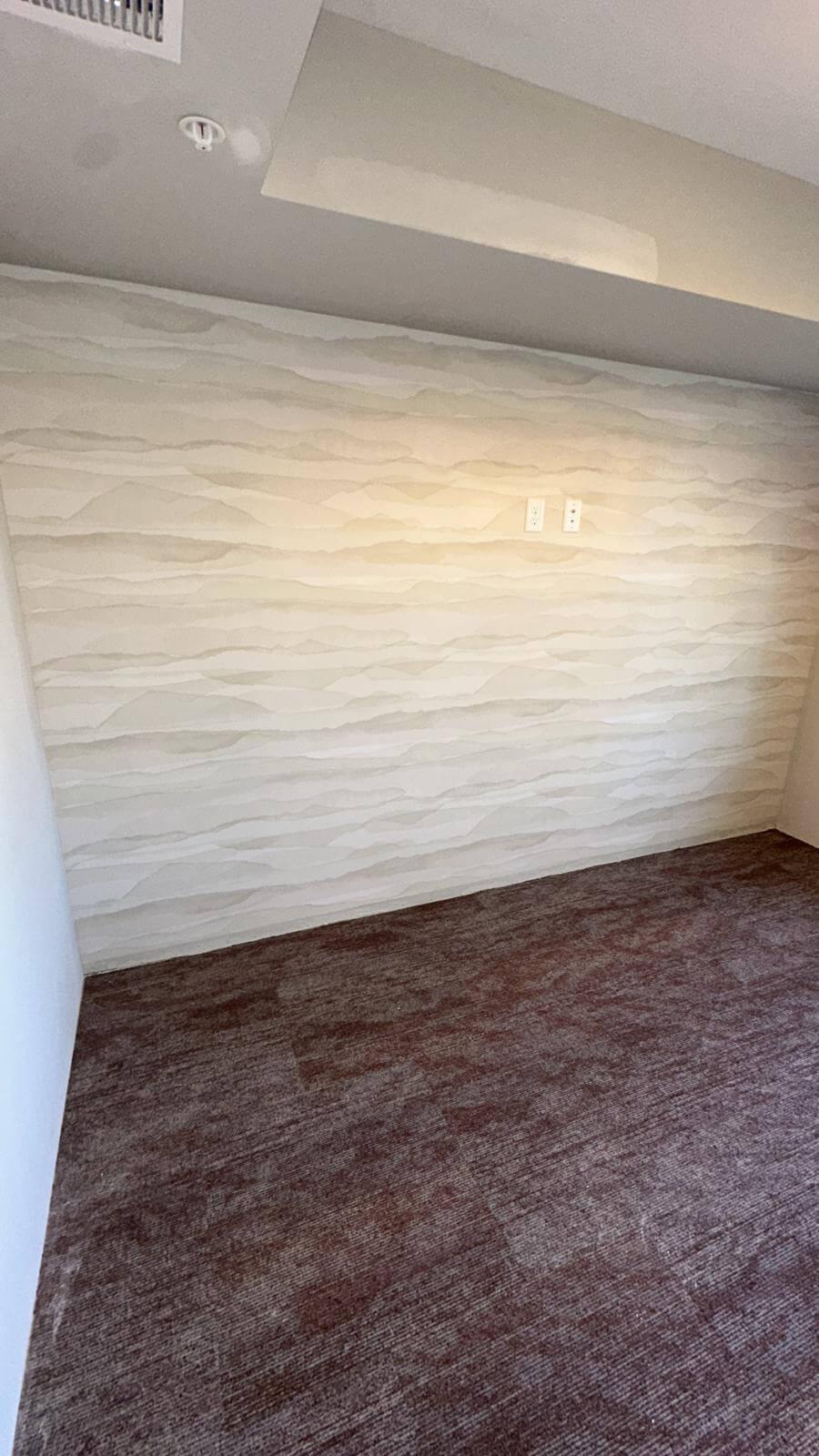 Wallpaper that looks like watercolor strokes of valleys or clouds in shades of gray on a wall.